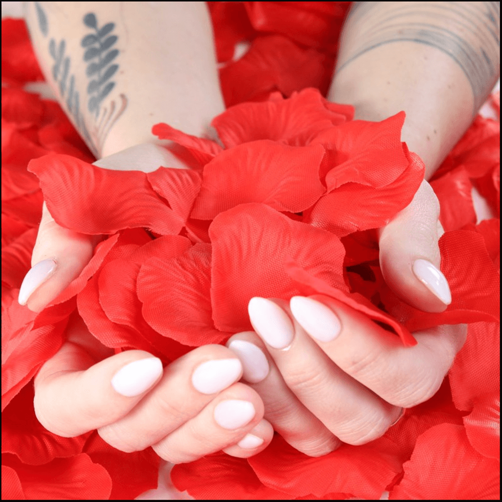 Hands holding bright red rose petals surrounded by more rose petals for romantic decoration