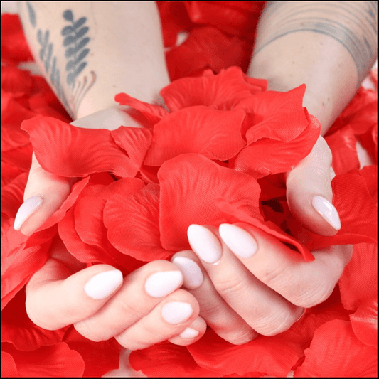 Hands holding bright red rose petals surrounded by more rose petals for romantic decoration